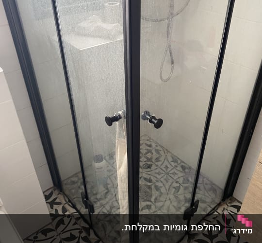 מקלחון פינתי מותקן עם פרופיל שחור ודלתות זכוכית בחדר רחצה